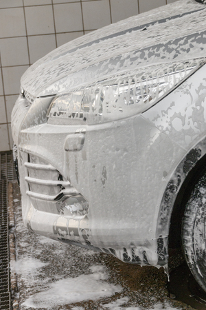 A Close up view of soap foam running off the front bonnet and side light of a sliver carの写真素材