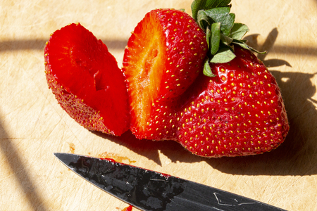 A close up view of a double headed strawberry where the one said has been cut with a sharp black knifeの写真素材