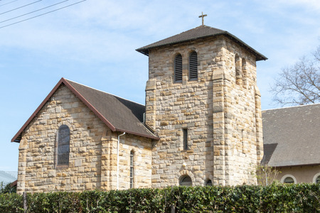 A side view of the top of a stone church with a green plant hedge over the main fence around the churchの写真素材