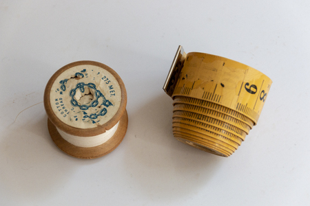 A close up view of a old wooden cotton bobben reel and an old measuring tape that has faded on a...