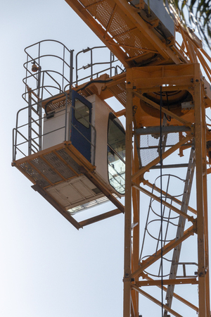 A close up view from the ground of the drivers cab of a yellow crane working on a construction siteの写真素材