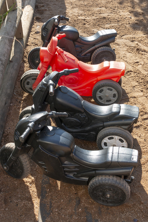 Four plastic kids bikes all in a row in a outside playground linned up in the sandの写真素材