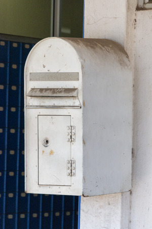 A close up front view of a white metal dirty post box that is bolted to the wall outside a post officeの写真素材