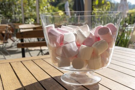 A close up view of pink and white marshmallows in a large round glass container on a wooden table