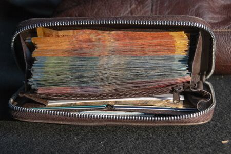 A close up view of pile of two hundred, one hundred and fifty rand sound african notes packed tightly in a brown leather walletの写真素材