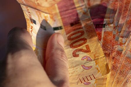 A close up view of a hand holding two hundred south african notes in a pile on a isolated black backgroundの写真素材