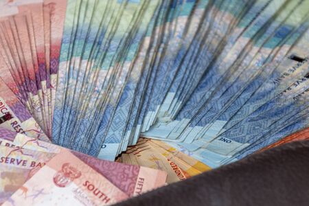 A close up view of pile of two hundred, one hundred and fifty rand sound african notes spread out next to a brown leathe walletの写真素材