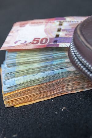 A close up view of pile of two hundred, one hundred and fifty rand sound african notes spread out next to a brown leathe walletの写真素材
