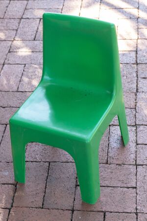 A close up front view of a green plastic chair on a brick pathwayの写真素材