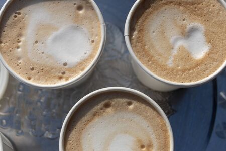 A close up top view of three open cups of cappuccino coffees on a silver trayの写真素材