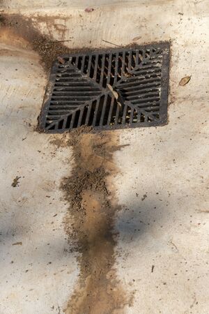 A close up view of dirt and sand that has dried leading to a metal grib leading to the drainsの写真素材