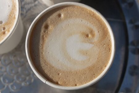 A close up view of the top of a open cups of cappuccino coffees on a silver trayの写真素材