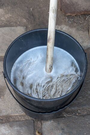 A close up view of a mop submerged in a plastic black bucket full of water and floor cleanerの写真素材