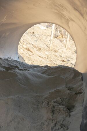 A close uop view of the inside on a black rubber pipe lying on the beach fulled with sandの写真素材