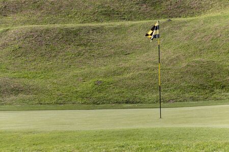 A close up view of a black and yellow flag pole, on the green at a hole on a golf courseの写真素材
