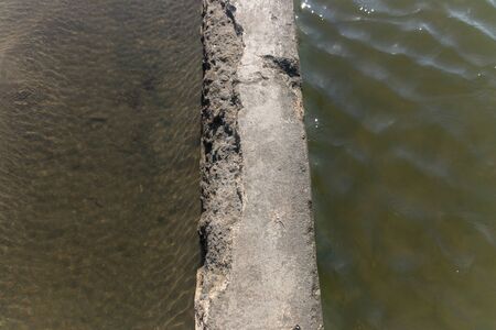 A close up view of a concete wall seperating two different sides of rocks pools at the beachの写真素材