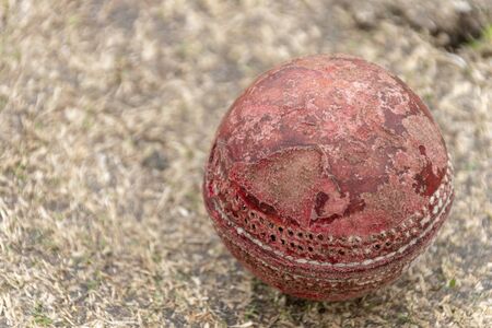 A close up view of a old well used red cricket ball on a grass pitchの写真素材
