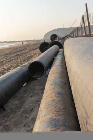 A close up view of large black rubber pipes waiting tobe layed into the sandの写真素材