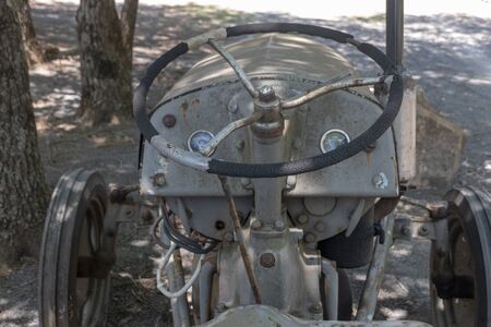 Durban-South Africa, November 2019- A close up view of old rusted tractor with a flat front tyre sitting in the field on a farmの写真素材