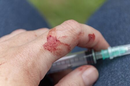 A close up view of a hand covered in blood holding a mecical saringe and needle in their handsの写真素材