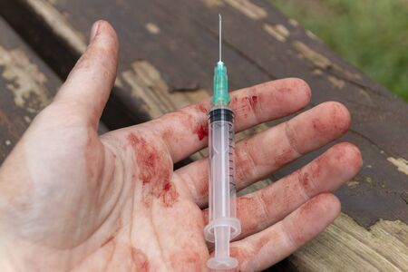 A close up view of someones open hand covered in blood holding a used mecical saringe and needle
