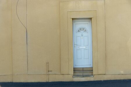 a close up view of a white front door where the wall around it in a mild yellow colourの写真素材