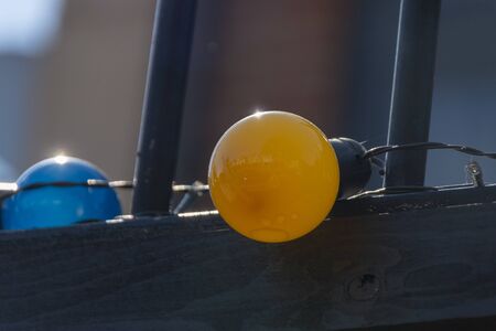 a close up view of a bright orange coloured light bulb connected to a row of differnat colours on the top of a fenceの写真素材