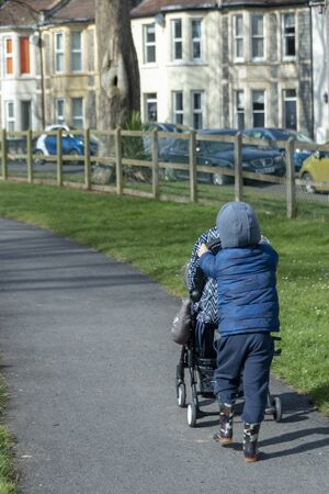 Bristol-March 2020-England a small boy pushing his young sibling in a pram or stroller around a...