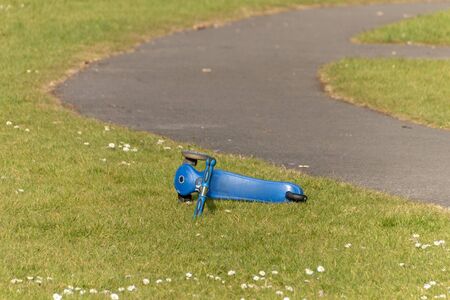 a close up view of a blue childrens scooter that has been left on the grass in a open public park