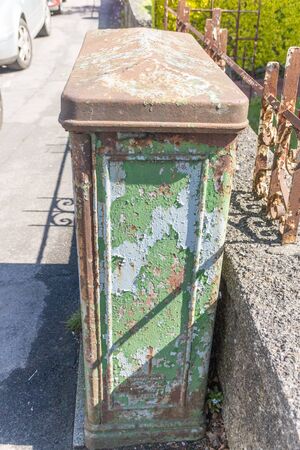 a close up view of a rusted old electrical box on the paving outside a building where the paint is peeling off.の写真素材