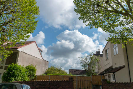 a close up view of the clouds in the blue sky though the middle of two buildings in a small villageのeditorial素材