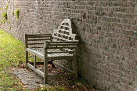 a close up view of a wooden bench that is placed next to a brick wall leading to the top of a large gardenの写真素材