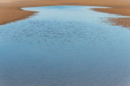 a close up view of the ripples in the sand from the low tide with a small water poolの写真素材