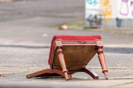 A close up view of a red velvet  broken wooden chair lying in the middle of the streetの写真素材