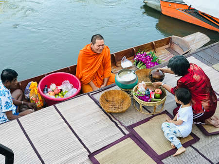 Samut Songkhram, Thailand - August 29, 2020:  The grandmother and grandchild are giving alms to a Buddhist monk in the paddle boat at the pier in Samut Songkhram, Thailand.のeditorial素材