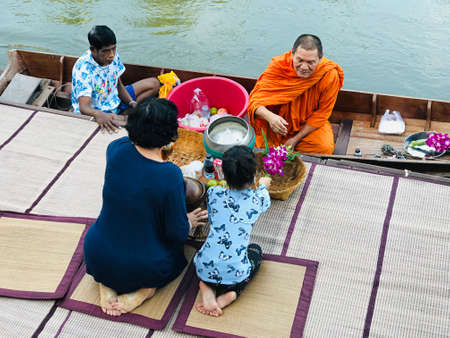 Samut Songkhram, Thailand - August 29, 2020:  The mother and daughter are giving alms to a Buddhist monk in the paddle boat at the pier in Samut Songkhram, Thailand.のeditorial素材