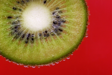 Closeup of a kiwi slice covered in water bubbles against a red backgroundの写真素材