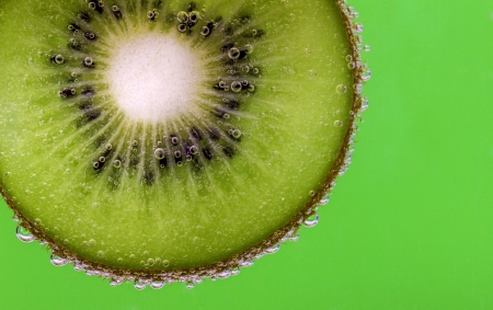 Closeup of a kiwi slice covered in water bubbles against a green backgroundの写真素材