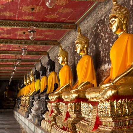 golden and black buddhas lined up along the wall of buddhist temple