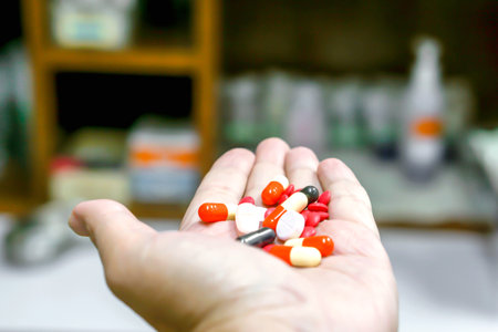 Capsule and medicine tablet on hand with blurry medicine cabinet background.