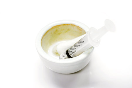 White liquid drug in a white ceramic cup and plastic syringe for injection to the patient isolate on...