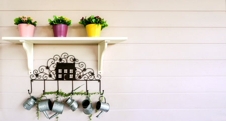 Flowers in three pots on a white shelf and hanging decoration small showers on white wooden wall...