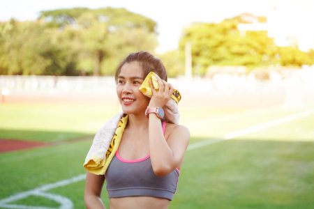 Young female relaxing after fitness training and jogging at the football stadium in the morning with sun flare.の写真素材
