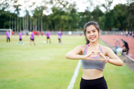 Young female wear a sportwear making a heart shaped hands at the football stadium in the morning. She have a beautiful smileの写真素材