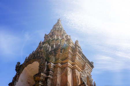 Look up view of traditional and ancient Thai Lanna art entrance gate of under bright blue sky with sun and lens flare background .の写真素材