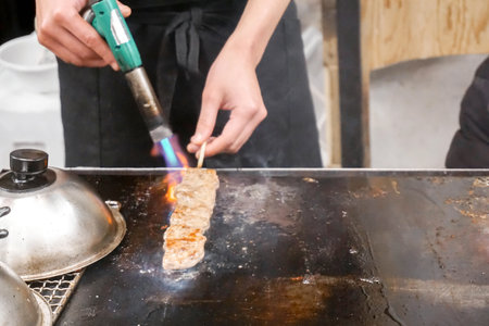 Hands of chef using burner cooking and burn Kobe beef stick on a hot pan to sale for customer at Kuromon market. Kobe beef stick Bar-B-Q is popular among tourists who come to Japan.の写真素材