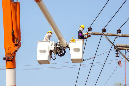 Electricians working on cable car to repair the power line under light blue sky background.の写真素材