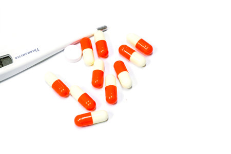 Capsule medicine of drug and electric medical thermometer on white background.