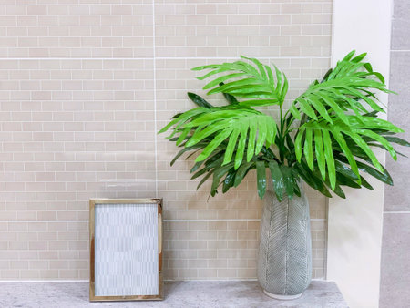 Ornamental plants in a ceramic vase with small picture frame on marble shelves and white tile in the toilet. with space for texts.の写真素材