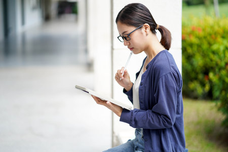 Closeup Asian young female student in casual cloth reading and make a short note on tablet for the exam at school building and blurred background. Asian school concept.の写真素材